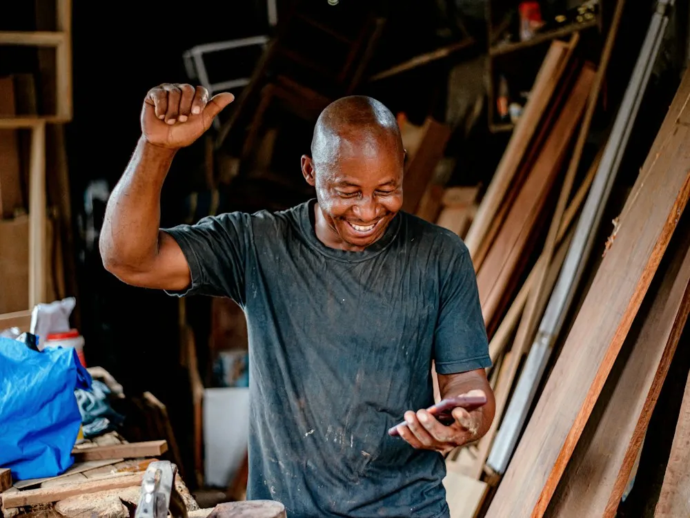 A tradesperson smiling at a notification on his phone in his workshop